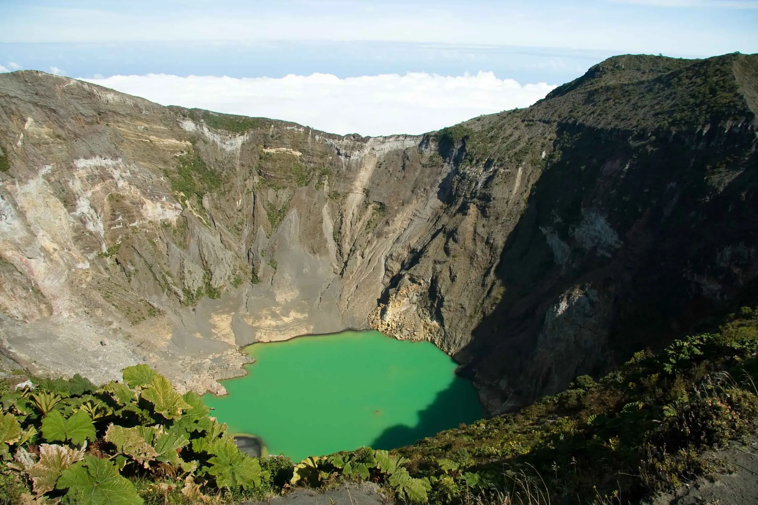 "Volcano crater with green water at the bottom, under a beautiful sunny day with clear blue skies."