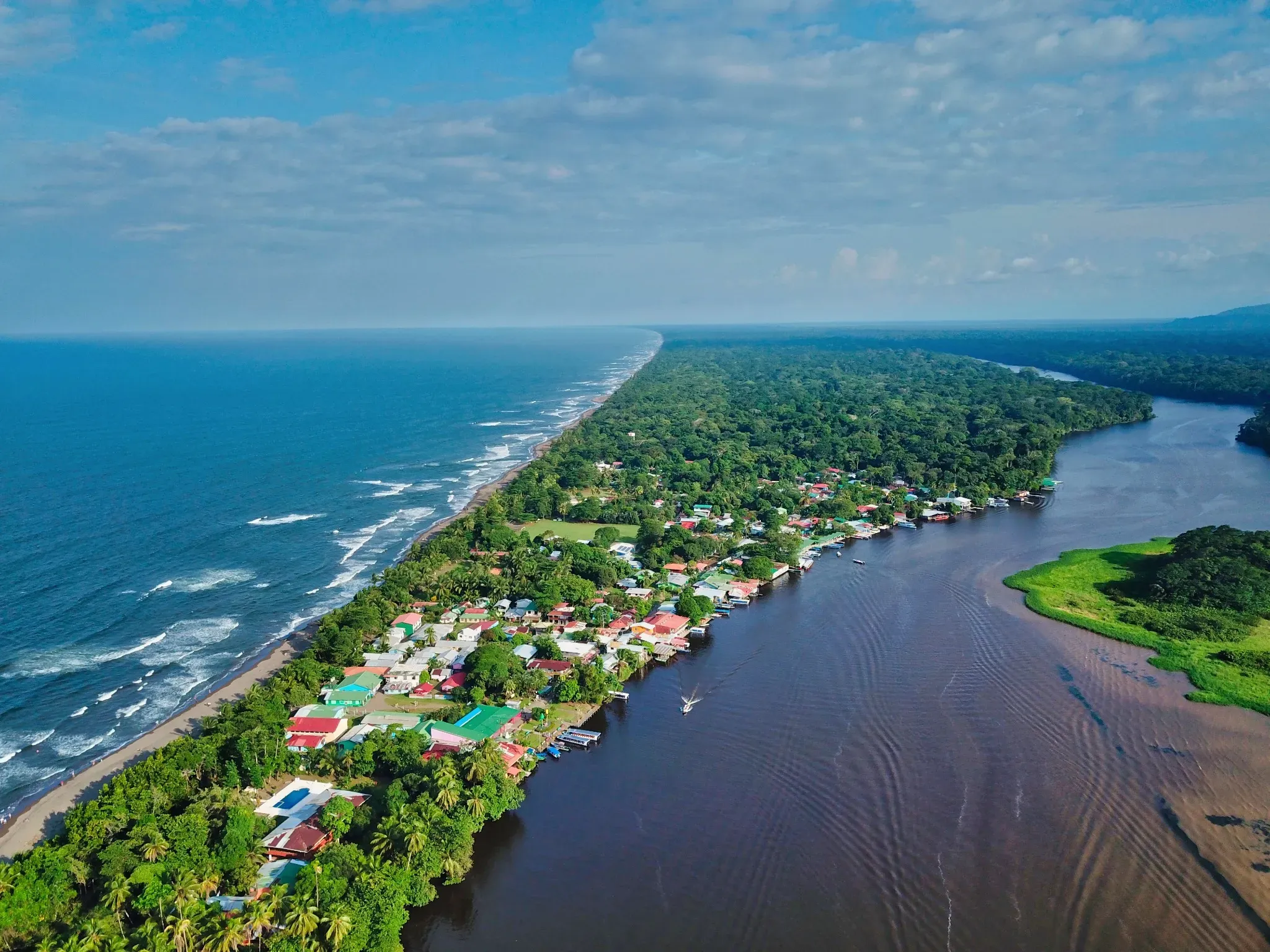 Aerial view of Tortuguero village in Costa Rica, nestled between the Caribbean Sea and a winding river, a unique crstours destination.