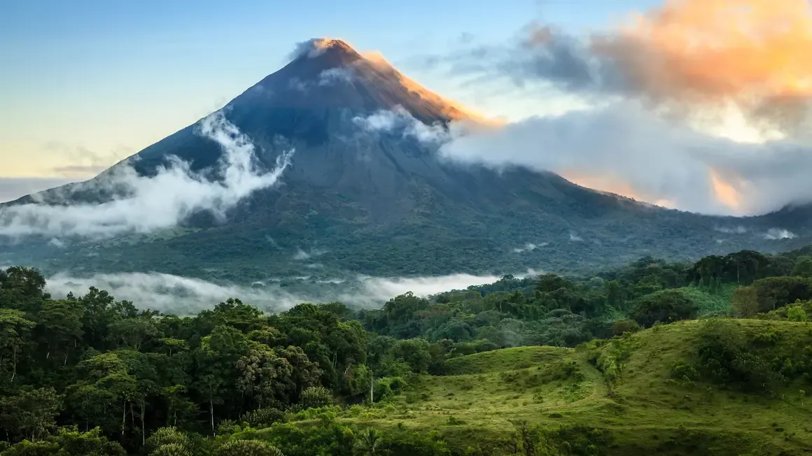 Arenal Volcano at sunrise rising above green hills and low clouds in Costa Rica