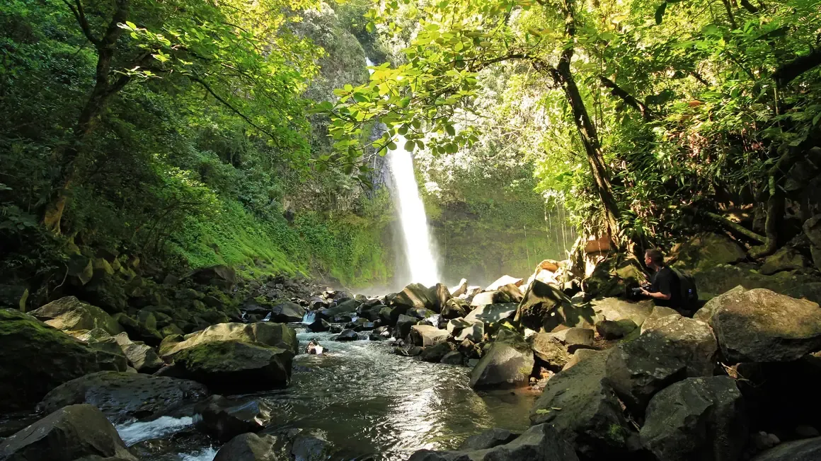 La Fortuna waterfall pouring into a rocky stream in the rainforest near Arenal
