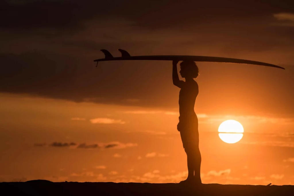 "Beautiful sunset with a young person holding a surfboard on their head, gazing at the colorful sky."