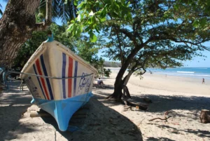 "Boat resting on the sandy shore in Tamarindo with a sunny sky and clear blue ocean in the background."