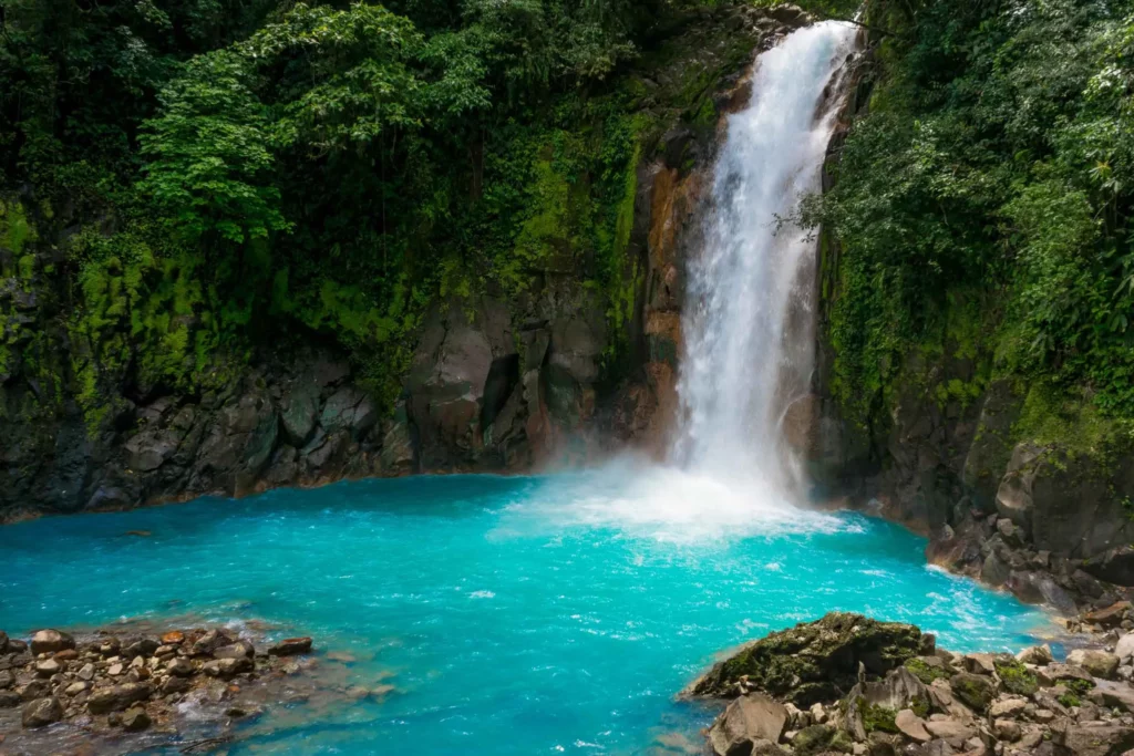 "Turquoise-blue Río Celeste flowing through a lush rainforest in Costa Rica, with its vibrant color contrasting against the surrounding greenery."