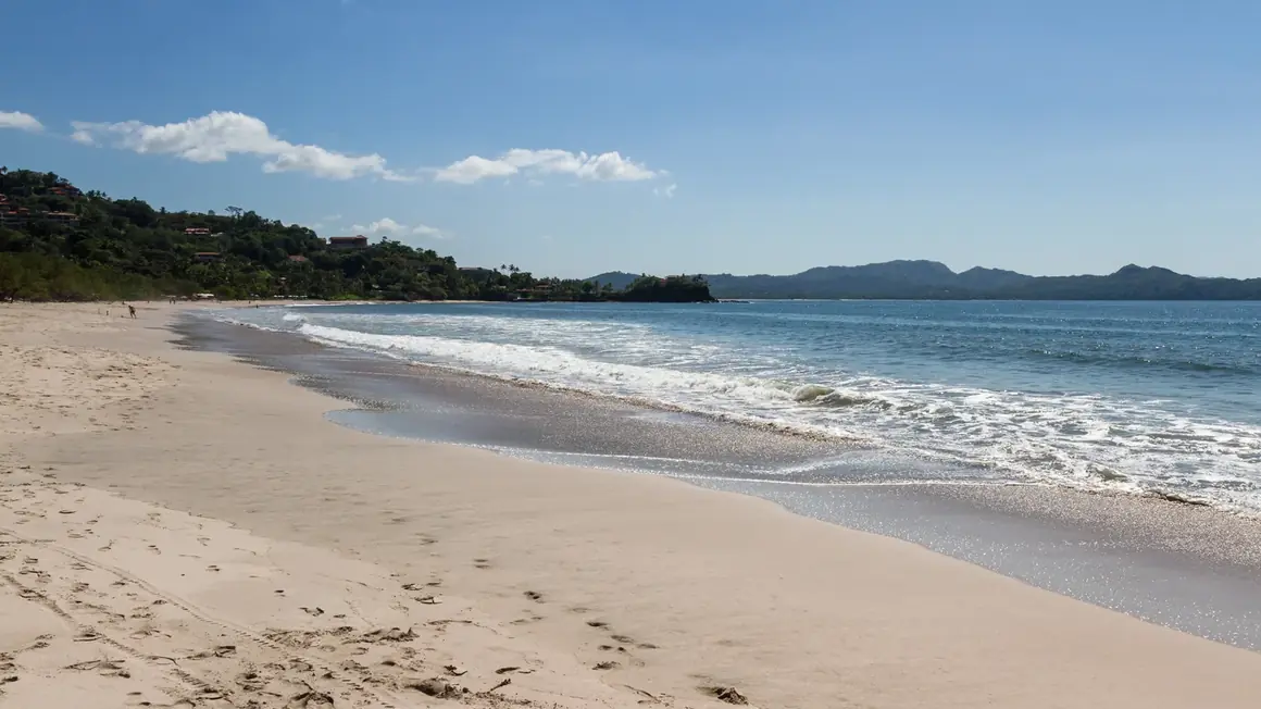 Spiaggia sabbiosa sulla costa del Guanacaste con onde leggere e colline verdi sullo sfondo