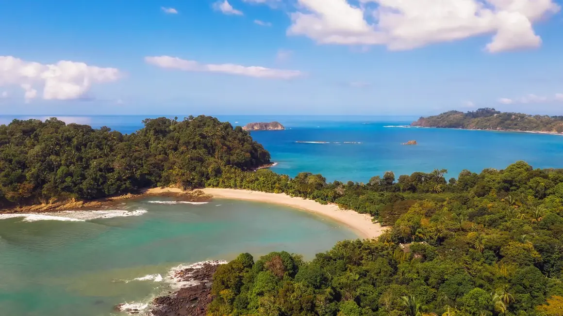 Veduta aerea di una baia sabbiosa nel Parco Nazionale Manuel Antonio, circondata da foresta pluviale e acque turchesi